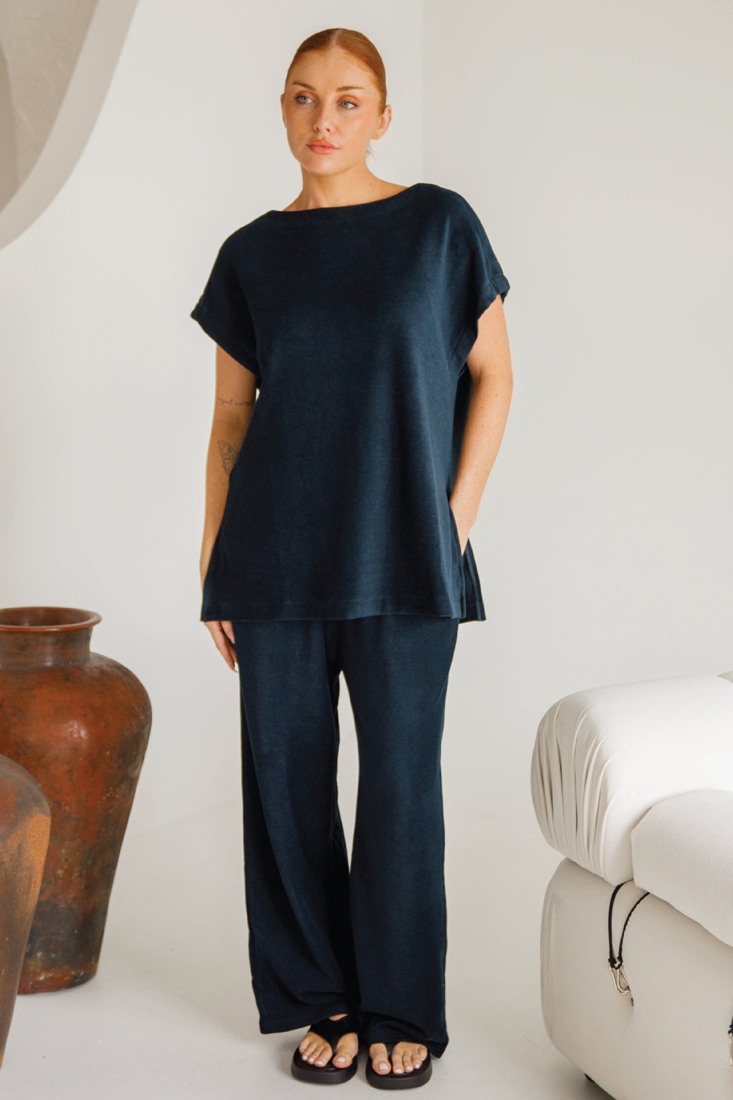 Woman wearing a dark blue outfit standing in a minimalistic room with white walls and a white couch.