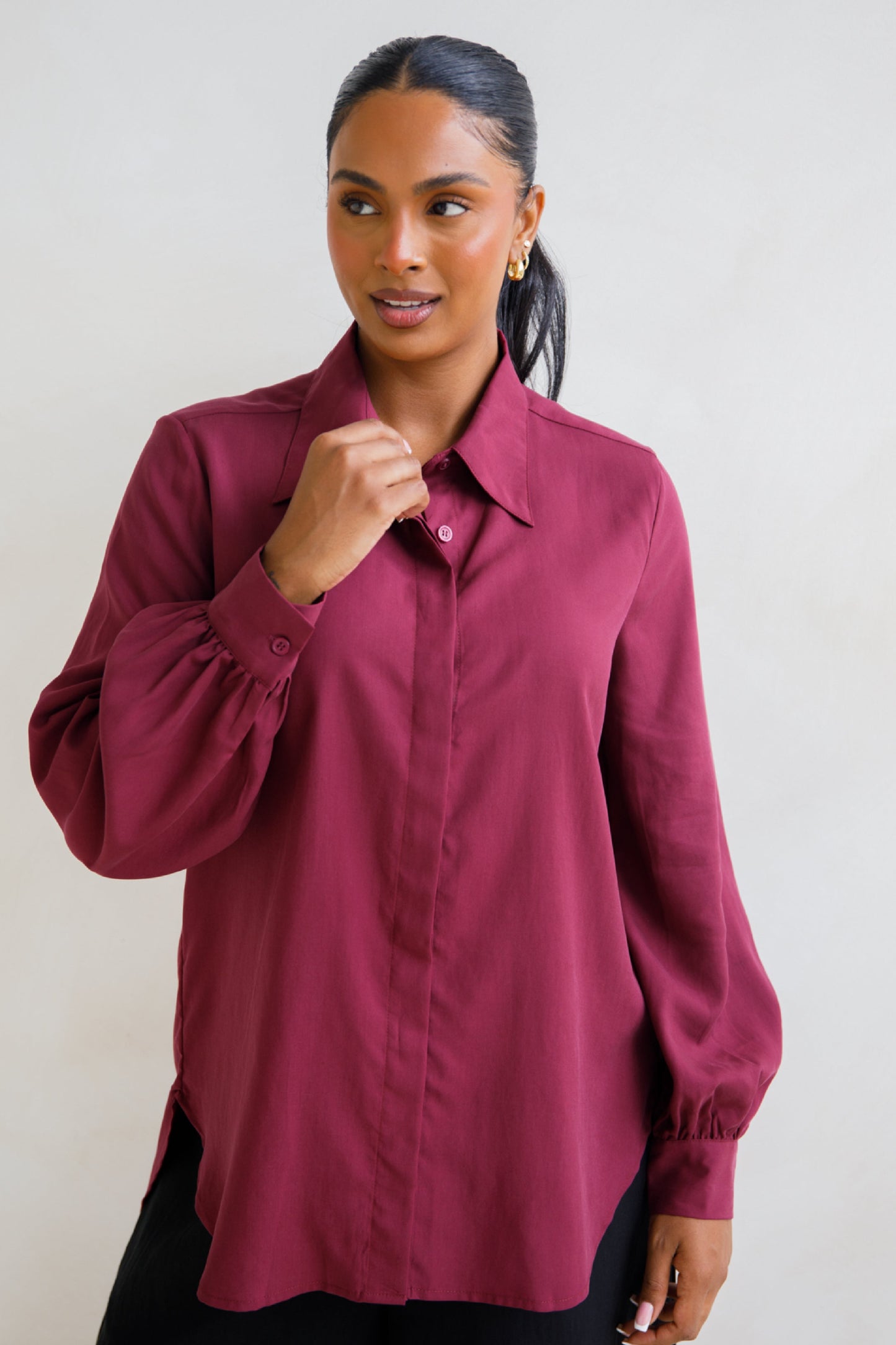 A woman wearing a long-sleeved, button-up maroon shirt with a collar.